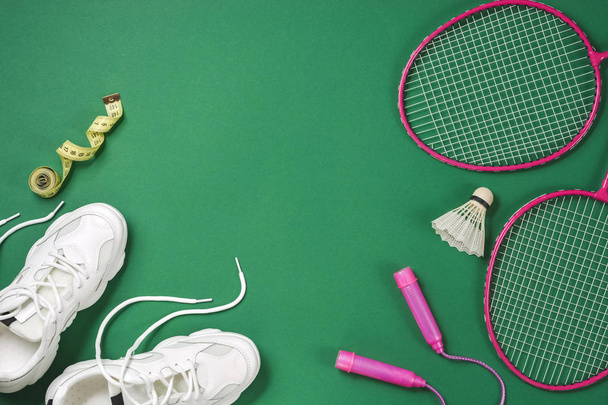 Sportflach lag mit Federball und Badmintonschläger, Springseil, Turnschuhen und Maßband auf grünem Hintergrund. Fitness, Sport und gesunder Lebensstil. - Foto, Bild