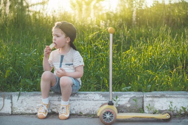 Happy Child eating and riding a scooter. Boy in the garden holding ice cream. Happy Boy kid eating ice cream. - 写真・画像