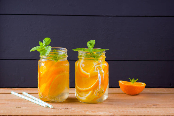 Infused water with orange, lemon and mint. Mug delicious refreshing drink of mix fruits with mint on wooden boards. Iced summer drink in mason jar. Homemade detox cocktail - Fotó, kép