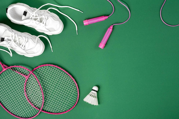 Sports equipment.. Shuttlecock and badminton racket, skipping rope, sneakers on green background. Fitness, sport and healthy lifestyle concept. - Фото, изображение