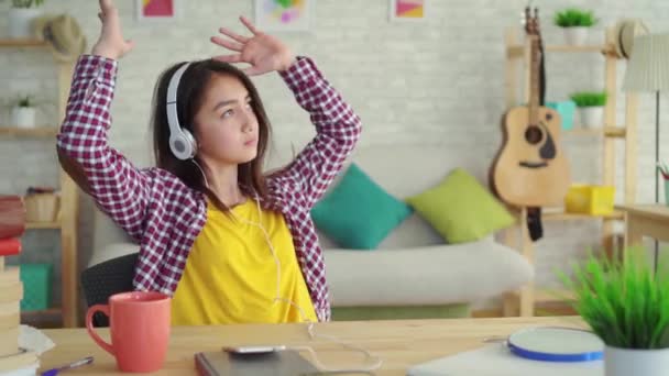 beautiful Asian girl with long hair in the living room of a modern house with headphones listening to music and relaxing - Materiał filmowy, wideo