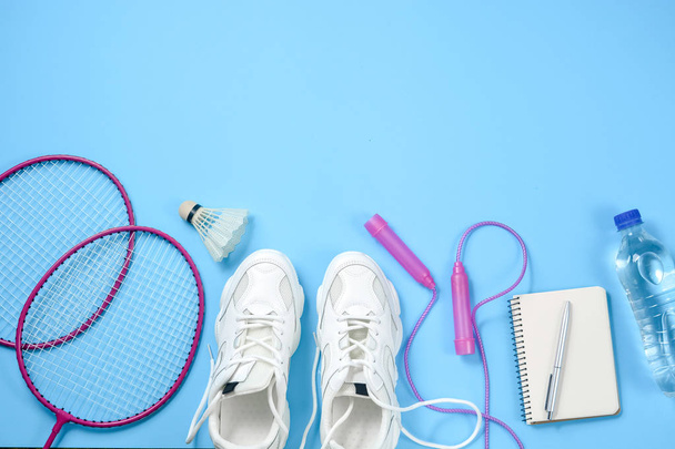 Sport equipment. Shuttlecock and badminton racket, skipping rope, sneakers, bottle water, pen and notepad on blue background. Fitness and healthy lifestyle concept.Flat lay, top view, copy space - Фото, изображение