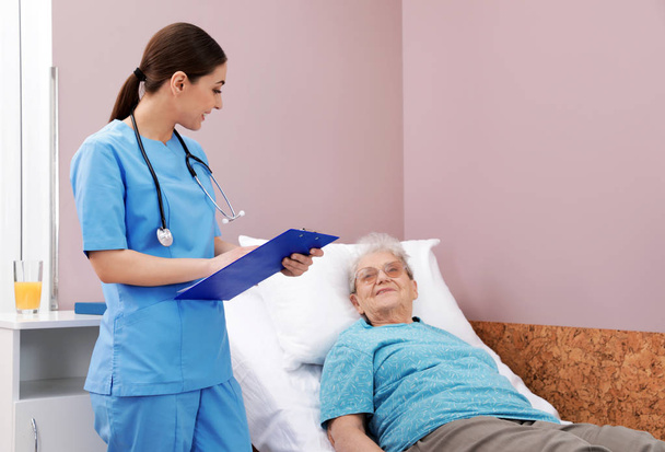 Nurse assisting senior woman lying on bed in hospital ward - 写真・画像