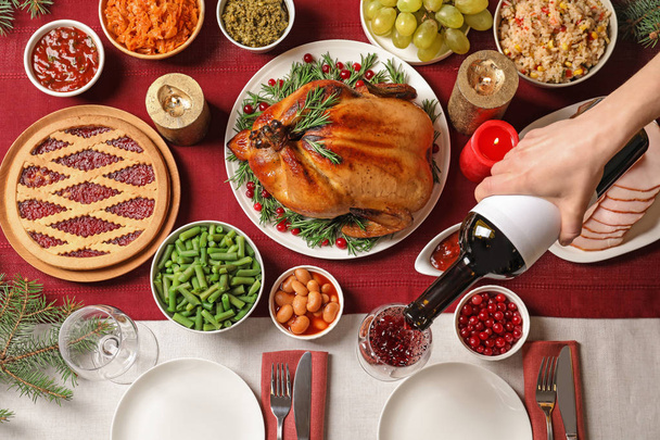 Woman pouring wine into glass at table with delicious roasted turkey for festive dinner, top view - 写真・画像