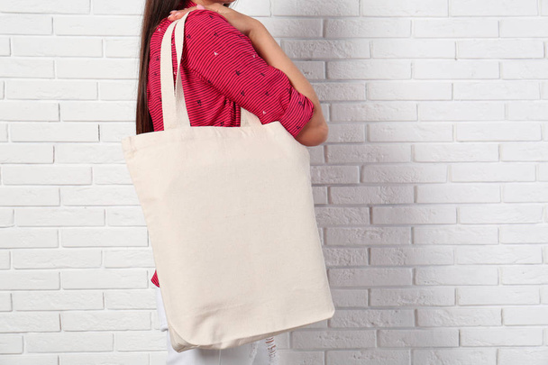 Woman with stylish blank eco bag near brick wall, closeup. Space for text - Foto, Bild