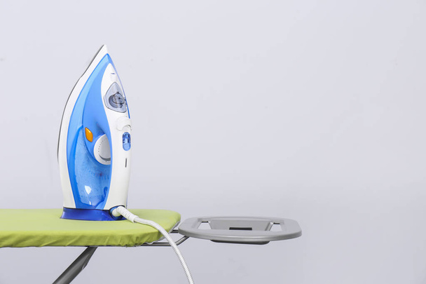 Modern electric iron on board against light background, space for text - Фото, изображение