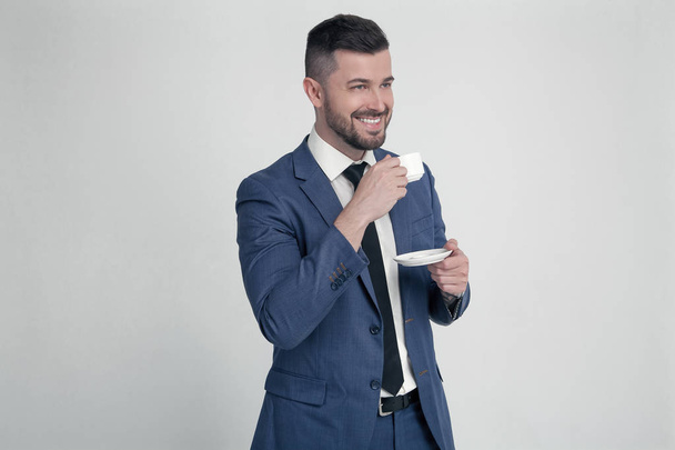 A businessman with a stylish hairstyle and beard keeps a cup of coffee and smiles, looks to the side where there is a free space for your logo or text. Isolated on a white background - Foto, imagen
