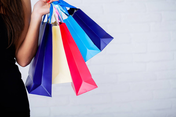 Compras. Primer plano de la mujer sosteniendo bolsa de compras de papel de color sobre fondo de pared blanco
 - Foto, imagen