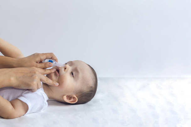 Küçük çocuk burun damlası alıyor. Pediatrist bebek burnuna tuzlu damla koyuyor. Anne elleri bebeğin burnunu temizliyor. 6 aylık çocuk burun damlaları alır. - Fotoğraf, Görsel