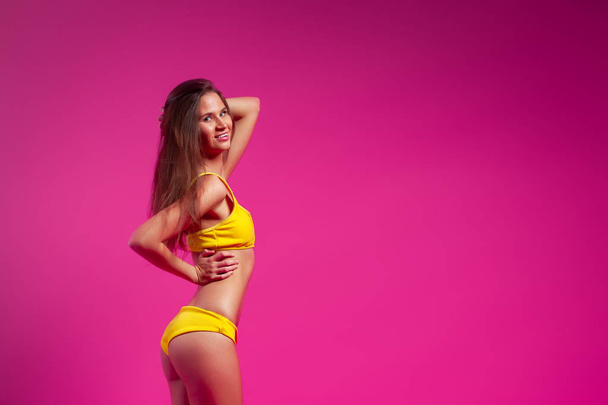 Beautiful woman with healthy body wearing in a yellow swimsuit on pink background.The concept of summer fashion swimsuit and relaxation. pink and joyful mood.  - Foto, Imagem