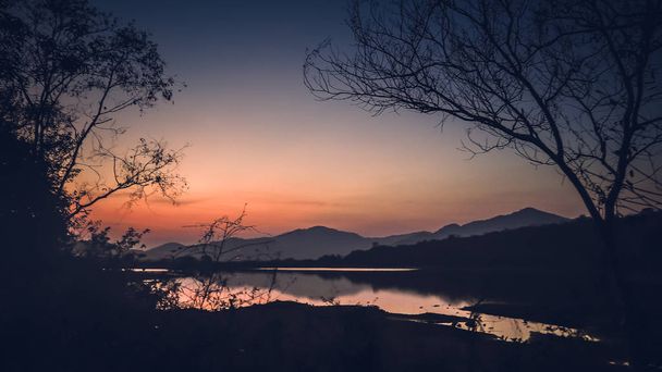 Landscape with orange and purple at sunset  silhouettes of mountains, hills and forest lake - 写真・画像