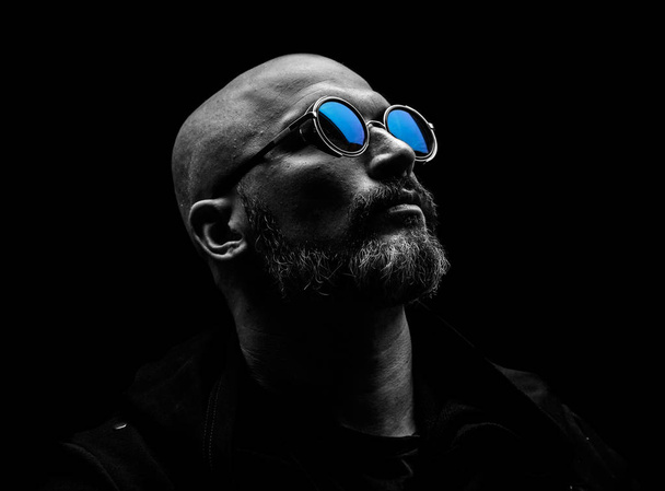 Bald man with grey beard in sunglass on dark background - 写真・画像