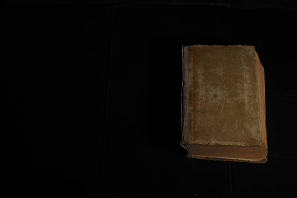 Vintage book with very old shabby cover on dirty black background with hard light and shadow.  - Photo, image