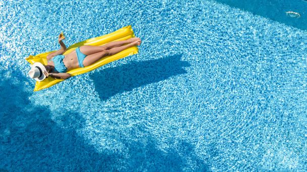 Beautiful young girl relaxing in swimming pool, swims on inflatable mattress and has fun in water on family vacation, tropical holiday resort, aerial drone view from above - Photo, image