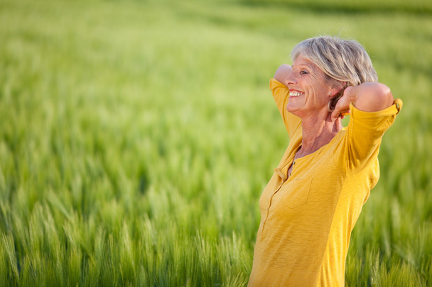 Senior vrouw met handen achter hoofd op gras veld - Foto, afbeelding