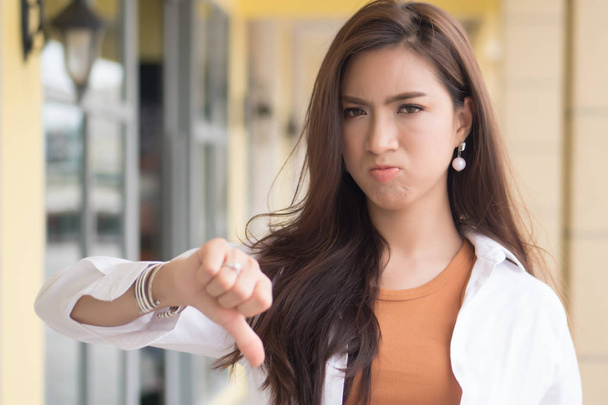 angry woman pointing thumb down; portrait of angry upset frustrated negative woman pointing up disapproval, no, bad, rejecting thumb down gesture; asian chinese woman young adult model - Photo, Image