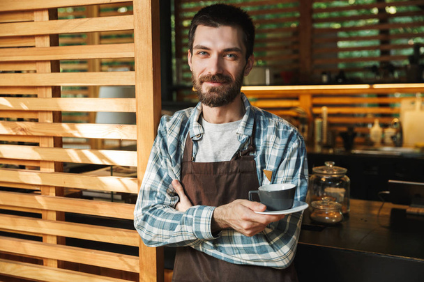 Retrato de tipo barista hombre sosteniendo la taza de café mientras trabaja
 - Foto, imagen