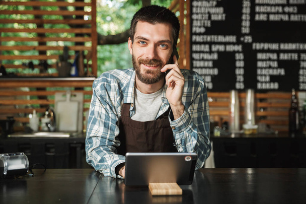 Portrait of cheery barista man using tablet computer while worki - Фото, зображення