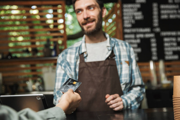 Portrait of young barista man taking credit card from customer w - Fotoğraf, Görsel