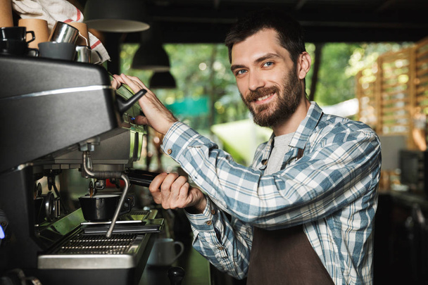 Image of smiling barista man making coffee while working in cafe - Foto, Imagem