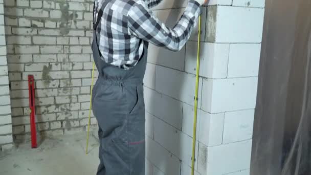 tilt shot of builder installing metal rails onto clamps on block wall - Materiaali, video