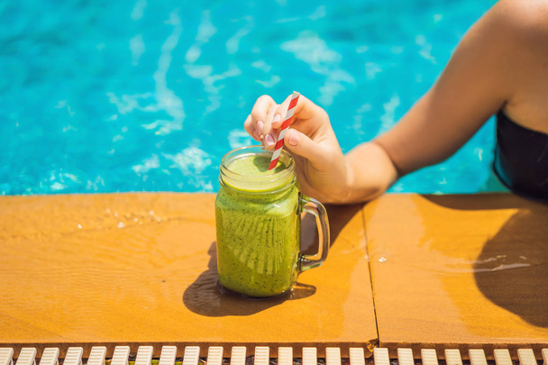 Woman with a green smoothies of spinach and banana on the background of the pool. Healthy food, healthy smoothies - Fotografie, Obrázek