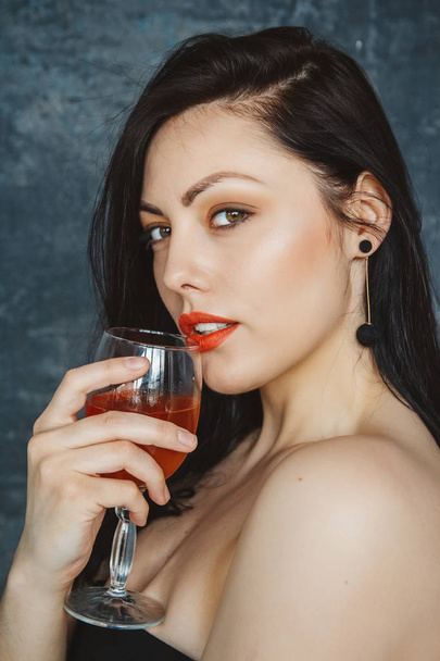 Krásná mladá žena se sklenicí vína na šedém pozadí. Pohled na kameru. - Fotografie, Obrázek