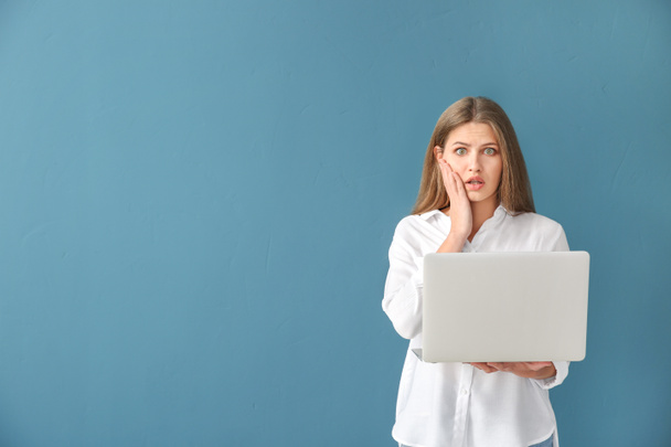 Shocked young woman with laptop on color background - Photo, image