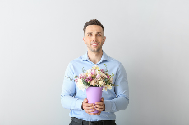 Handsome man with bouquet of beautiful flowers on light background - Photo, Image