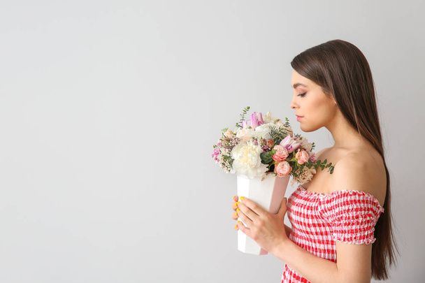 Beautiful young woman with bouquet of flowers on light background - Valokuva, kuva