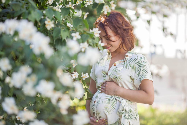 Beautiful young happy pregnant woman is standing near the blossoming tree. Motherhood. Love. Spring. - Photo, Image