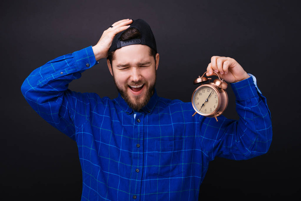Young bearded man holding an alarm clock and being late making a forget gesture. - Photo, Image
