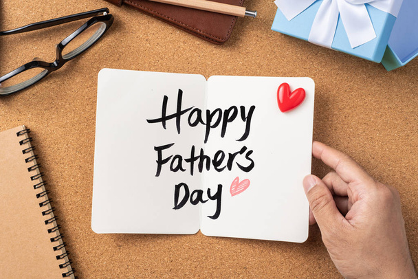 Fathers day layout with man hand holding white greeting card, ribbon kraft gift box on cork board background, copy space. - 写真・画像