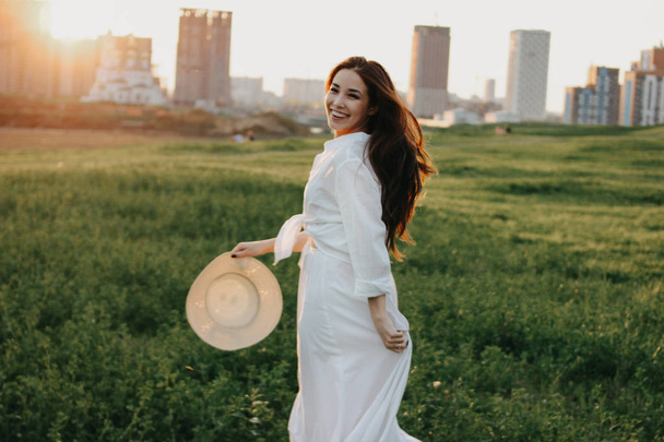 Belo cabelo longo despreocupado menina asiática em roupas brancas e chapéu de palha goza de vida no campo da natureza ao pôr do sol. Sensibilidade ao conceito de natureza
 - Foto, Imagem