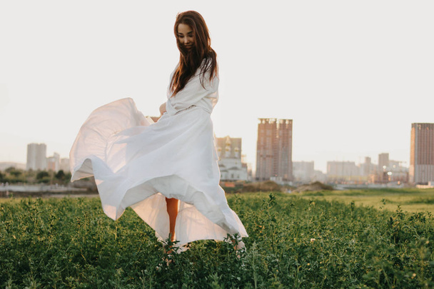 Kaunis huoleton pitkät hiukset aasialainen tyttö valkoisissa vaatteissa ja olkihattu nauttii elämästä luontoalalla auringonlaskun aikaan. Herkkyys luonnon käsitteelle
 - Valokuva, kuva