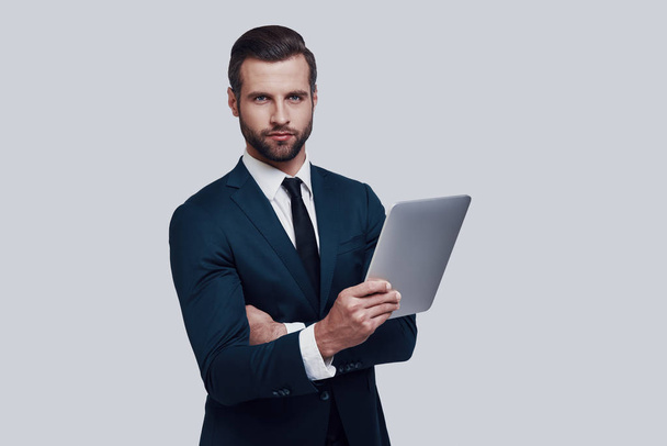 Geschäfte machen. schöner junger Mann, der vor grauem Hintergrund mit digitalem Tablet arbeitet - Foto, Bild