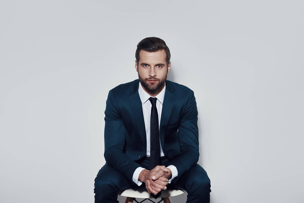 Perfect in every way. Handsome young man looking at camera while sitting against grey background - Photo, Image