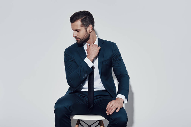 Overworked. Handsome young man pulling his collar while sitting against grey background - Foto, imagen