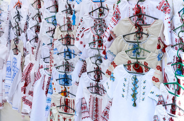 Ukraińskie Haftowane koszule, krajowe ręcznie robione ubrania. Tradycyjna koszula lniana z haftowane kwiaty i ozdoby na lokalnym rynku na targach państwowych. Targi-wystawa rzemieślników ludowych na otwartym powietrzu. - Zdjęcie, obraz