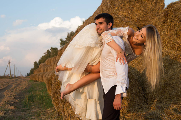 groom carries bride on shoulder along haystack - Zdjęcie, obraz