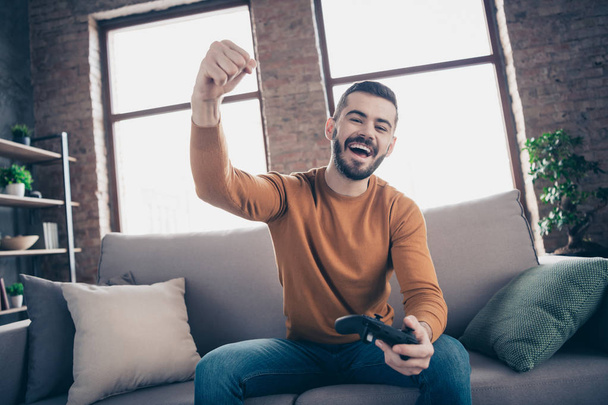 Portrait of his he nice-looking attractive bearded cheerful cheery glad guy spending weekend sitting on divan winning xbox entertainment at industrial loft brick interior style living-room indoors - Foto, afbeelding