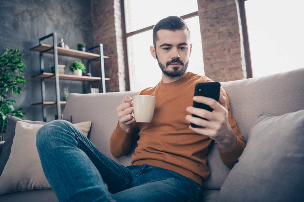 Low below angle view portrait of his he nice-looking attractive confident content freelancer bearded guy drinking latte writing sms at industrial loft brick interior style living-room - Φωτογραφία, εικόνα