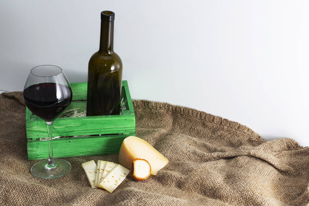 Бутылка красного вина со стаканом и кусочком сыра. - Фото, изображение