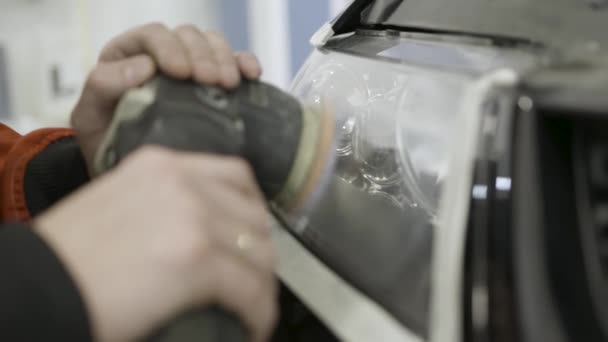 Close up for auto mechanic buffing and polishing car head. light. Art. Worker polishing the headlight of a car at automobile repair and renew service station, using a professional power buffer machine - Footage, Video