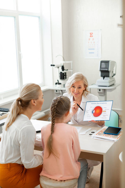 Beaming blonde ophthalmologist carrying detailed poster and talking - Foto, immagini