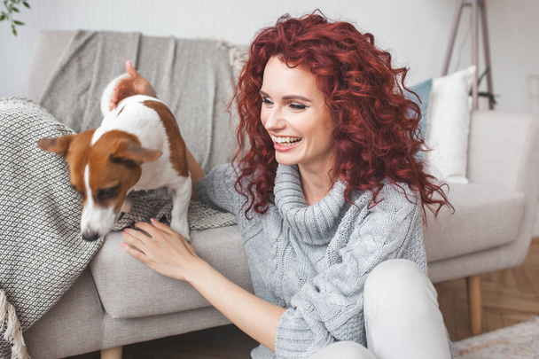 Jovem mulher atraente brincando com seu pequeno cão bonito. Feminino treinando seu animal de estimação em casa
.  - Foto, Imagem