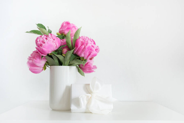 Bouquet of pink peony in vase with gift on white. Copy space for text. Mothers day. - Photo, Image