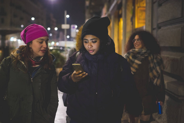 группа молодых женщин, идущих по улице и взаимодействующих со смартфоном
 - Фото, изображение
