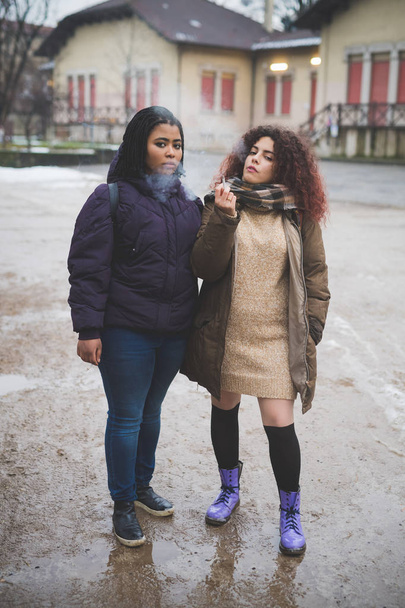 duas jovens mulheres fumando cigarro e olhando câmera -
 - Foto, Imagem