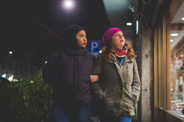 dwie wielorasowe kobiety spacerujące po ulicy i patrzące na witryny sklepowe - Zdjęcie, obraz